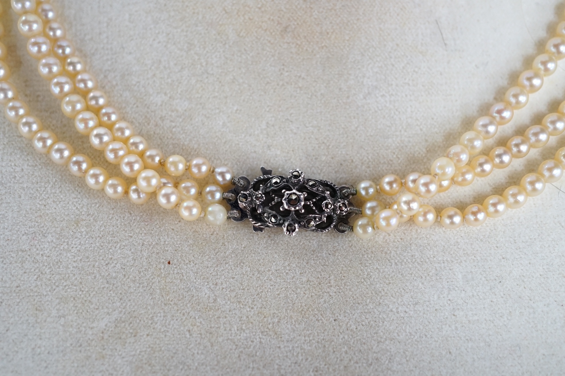 A triple strand graduated cultured pearl necklace, with marcasite set white metal clasp, 40cm. Condition - fair to good.